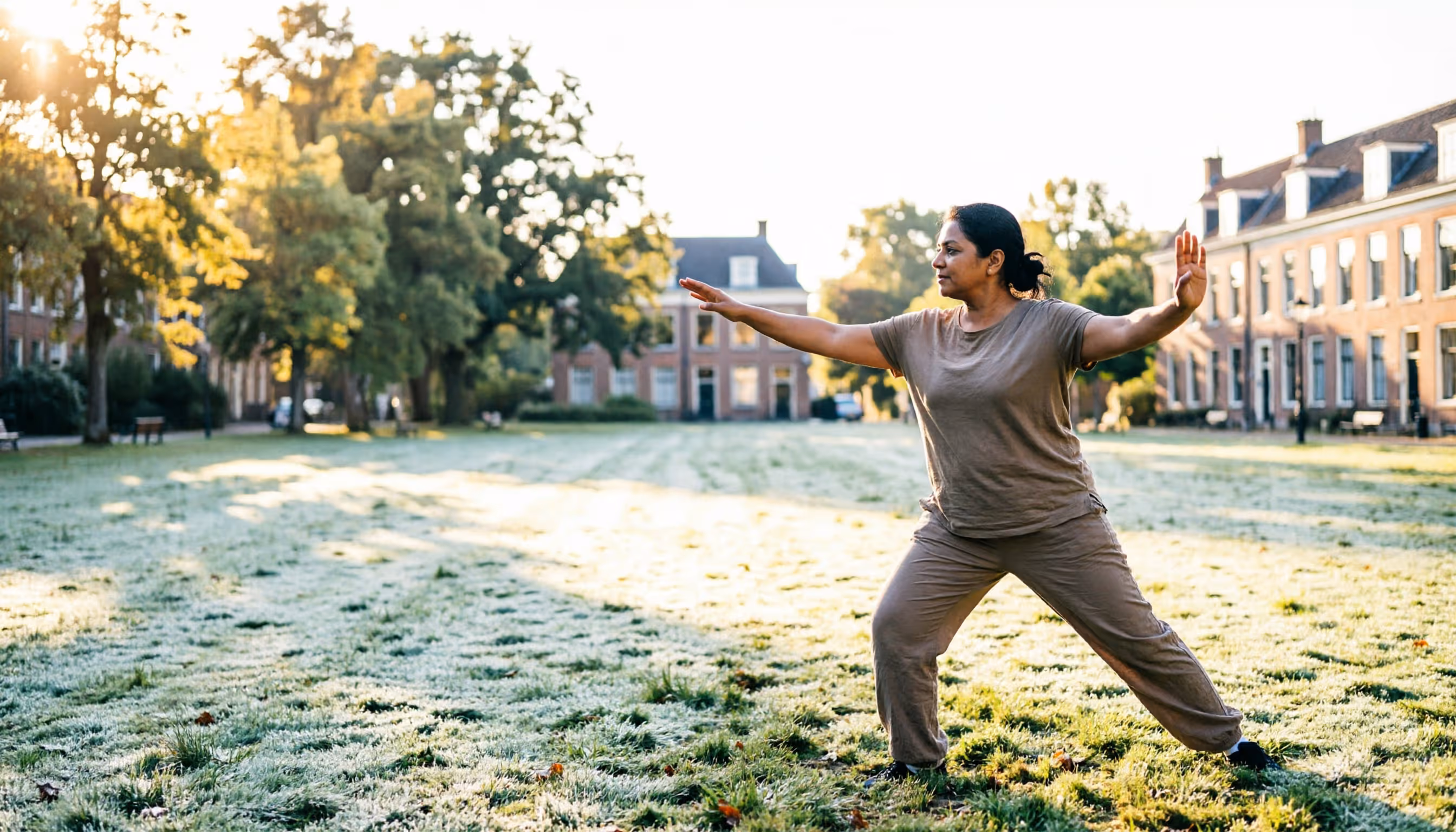 Een vrouw van begin veertig doet 's ochtends rustig tai chi in een zonnig Nederlands stadspark