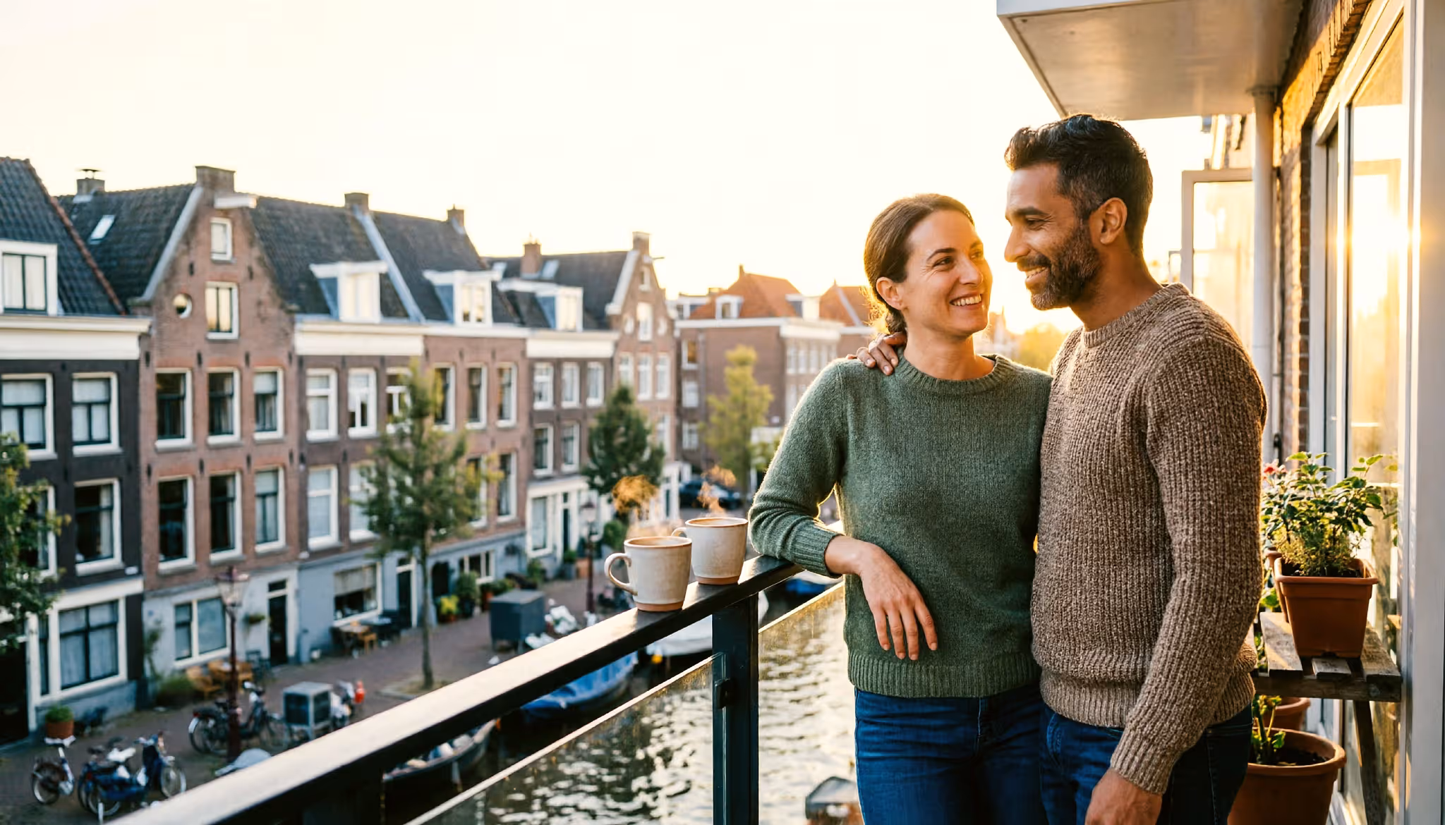 Een stel ontspant samen op het balkon van hun Amsterdamse appartement in het gouden avondlicht