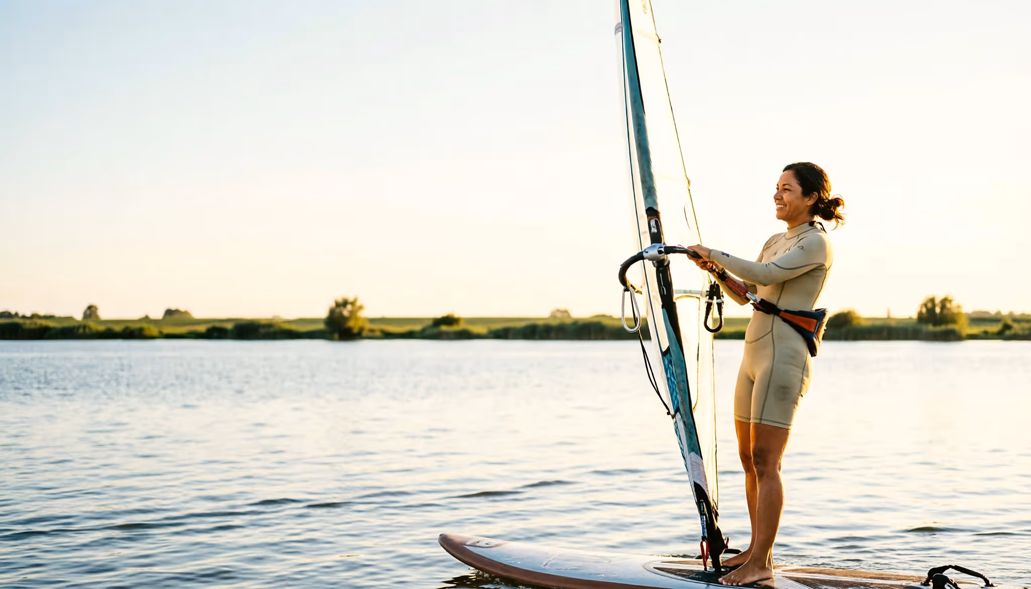 Een vrouw windsurft ontspannen over een kalm Nederlands meer in warm middaglicht