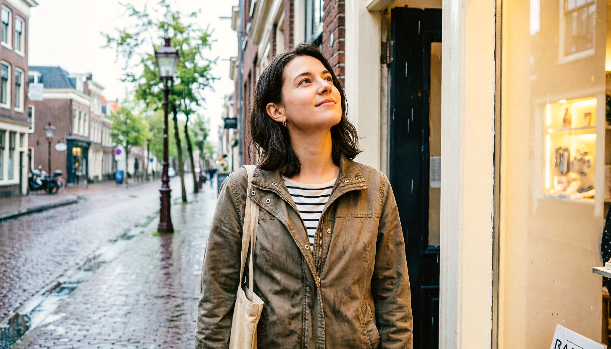 Een vrouw van eind twintig wacht een voorjaarsbui af in een winkelportiek in een Nederlandse stad