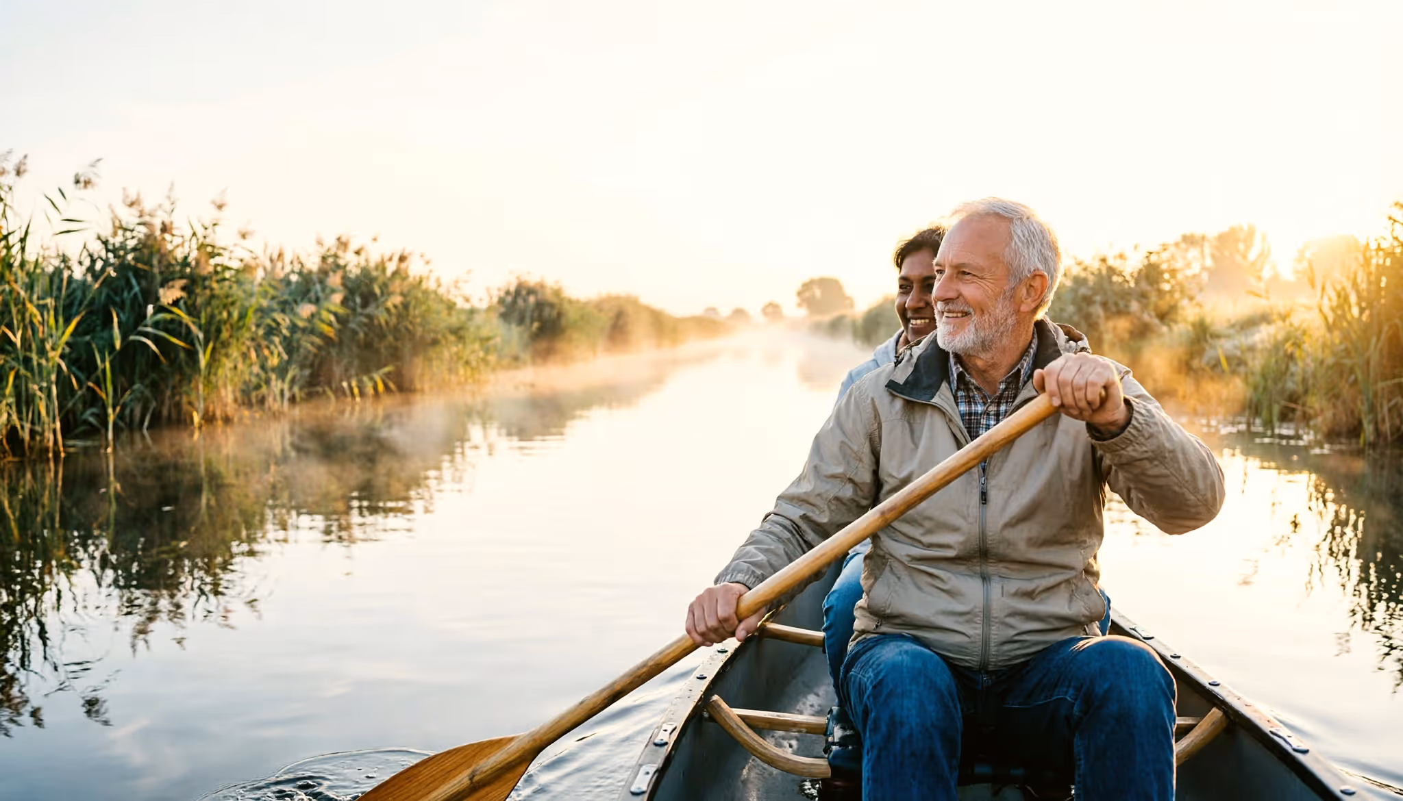 A retired couple in their sixties paddling a canoe on a calm Dutch canal at sunrise