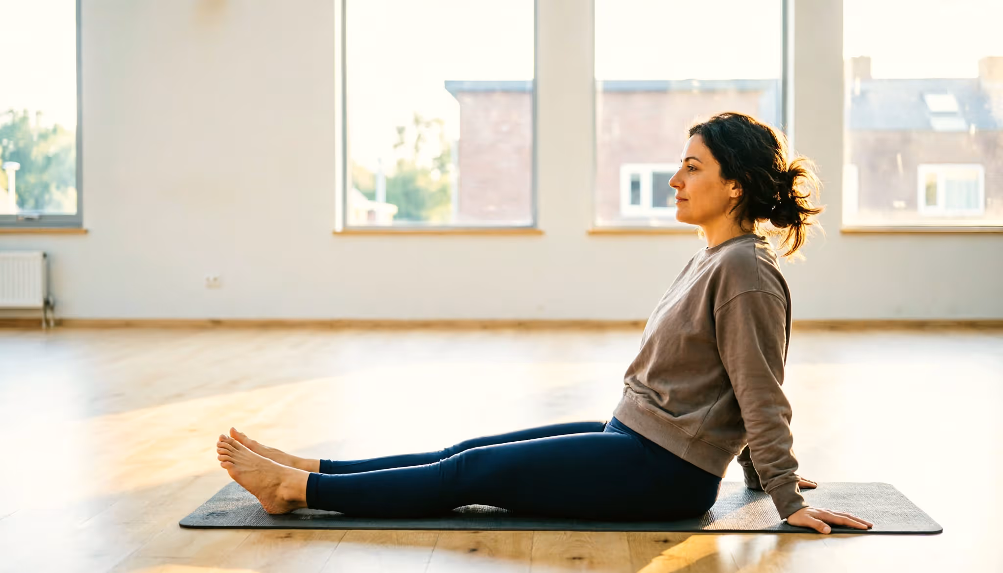A woman sits back on her mat at the end of a pilates class in a bright Dutch sports hall