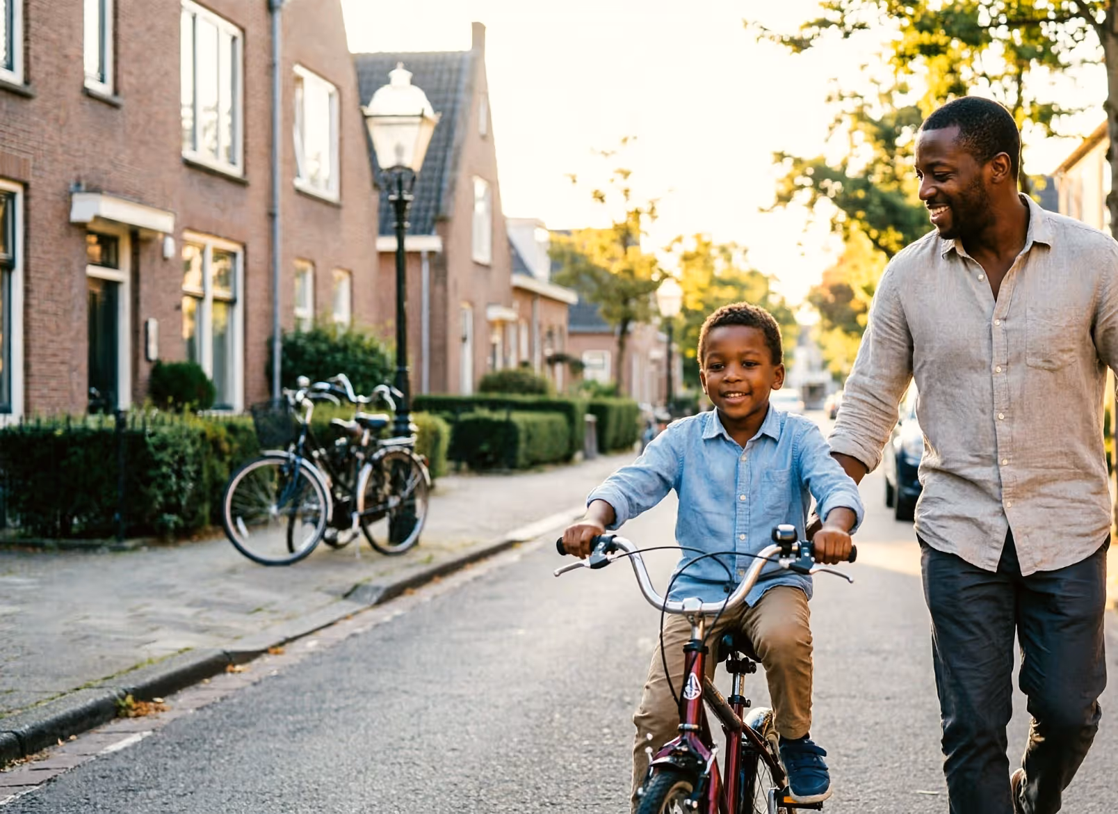 Een vader rent mee terwijl zijn jonge kind leert fietsen op een rustige Nederlandse straat