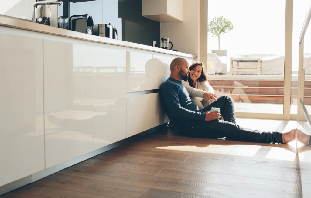 Young man and woman sitting on floor in kitchen and talking. Loving young couple spending time together at home.